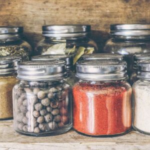 A collection of assorted spices in glass jars on a rustic wooden shelf for culinary use.